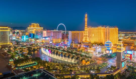 Cityscape of Las Vegas at night with illuminated buildings and a Ferris wheel.